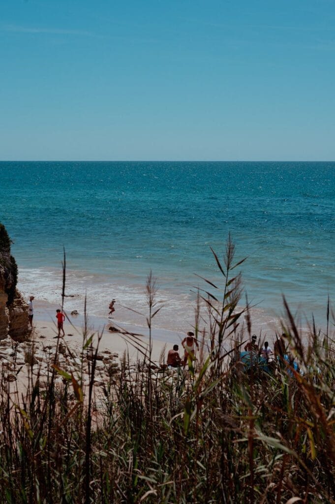 Serene beach scene with turquoise waters, rocky cliffs, and people enjoying the summer day.