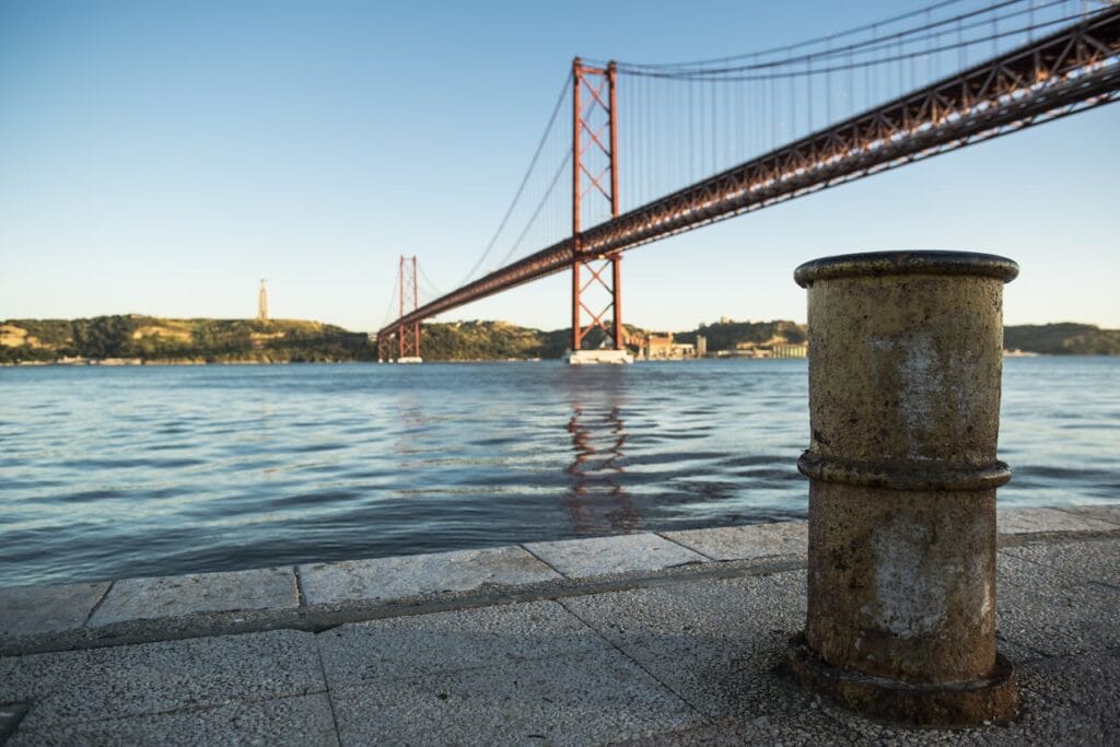 View of the 25 de Abril Bridge over the Tagus River in Lisbon at sunset with tranquil waters.